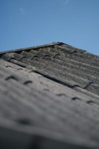 Sunlight falls across weathered shingles while loose granules collect in a roof gutter.