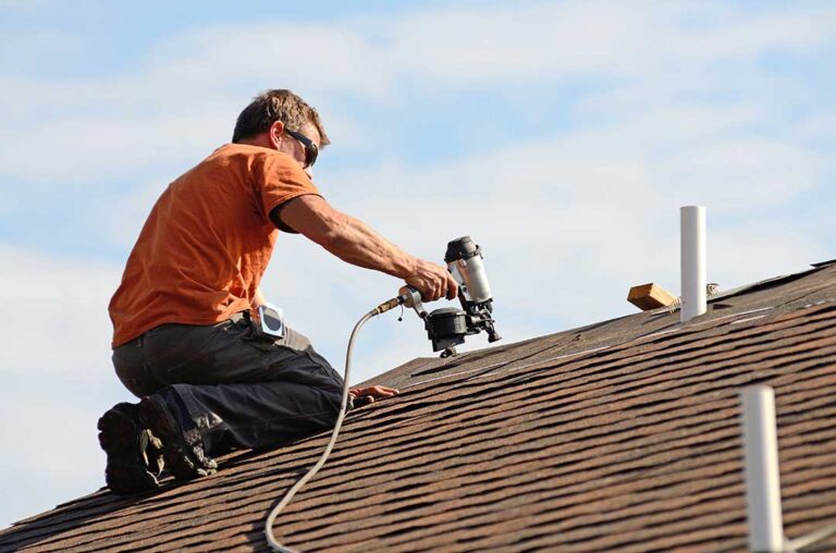 Homeowner inspecting clear gutters and a downspout directing rainwater away from a house